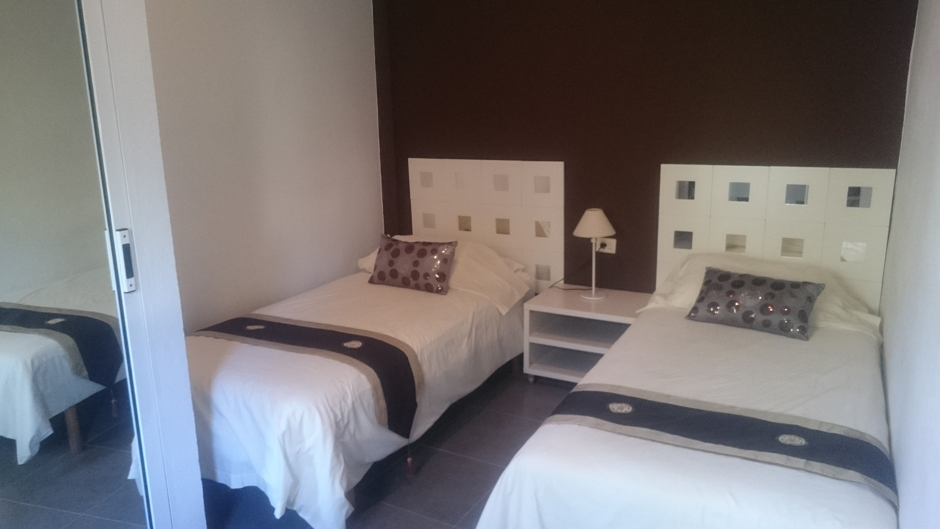 Een hotelkamer met twee eenpersoonsbedden, elk met een kussen en een nachtkastje met een lamp.