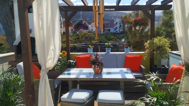 Un patio al aire libre con mobiliario de mimbre, una mesa y plantas en macetas.