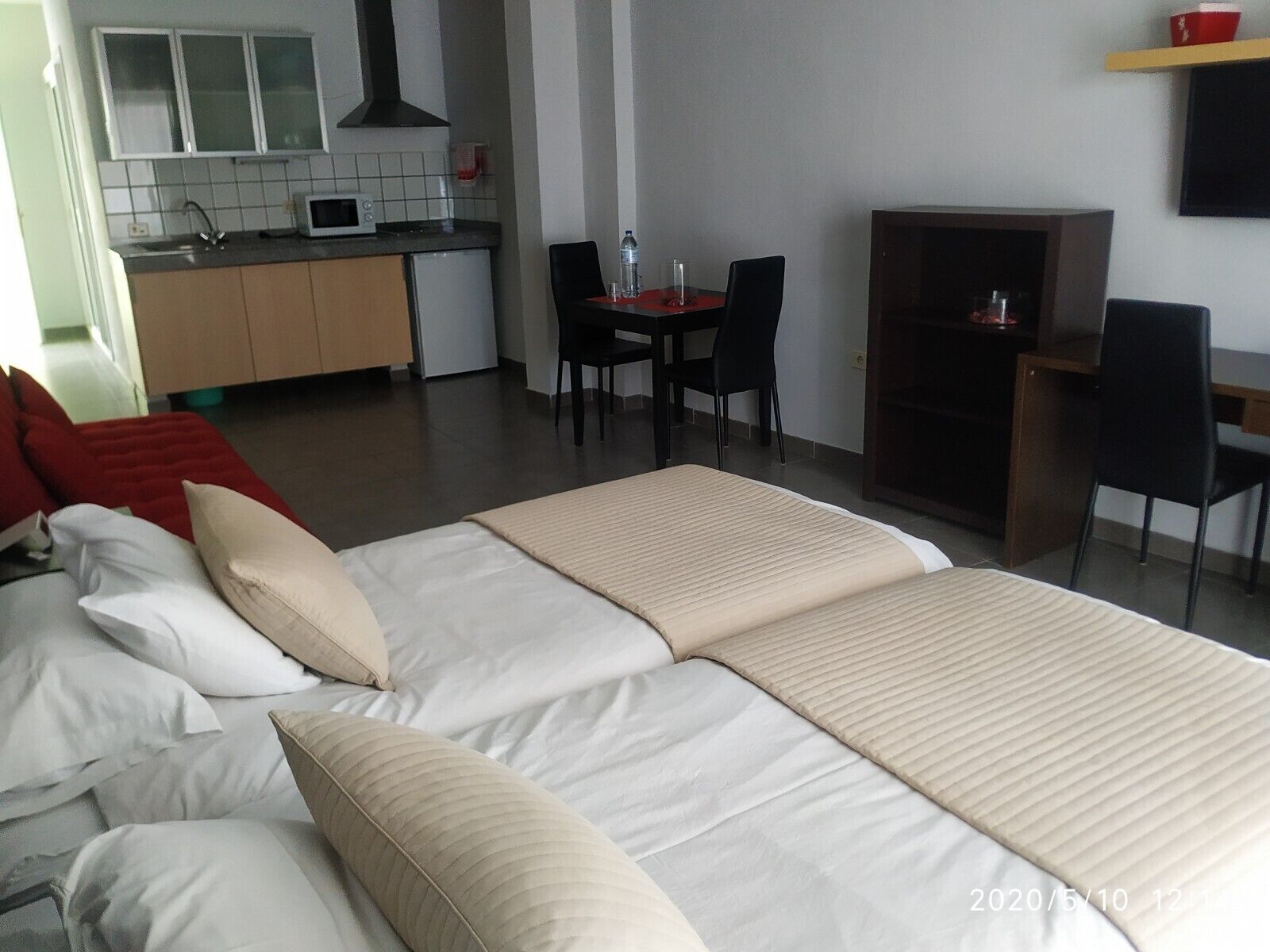 A hotel room with a bed, a desk, a chair, a small table, a microwave, and a kitchenette.