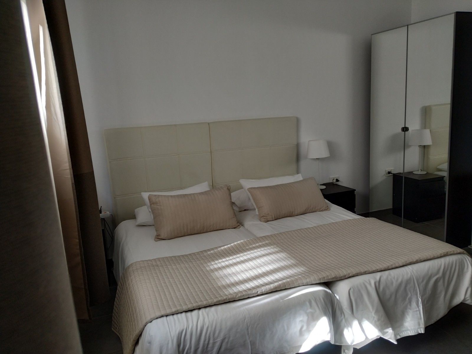 A hotel room with a large bed, two bedside tables, a nightstand, and a mirror.