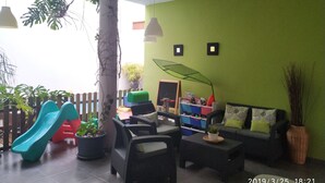 Una habitación con pared verde, un tobogán, muebles de mimbre y plantas en macetas.