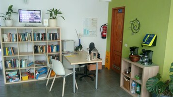 Una oficina en casa con escritorio, silla, estantería, monitor de computadora y diversos artículos de oficina.