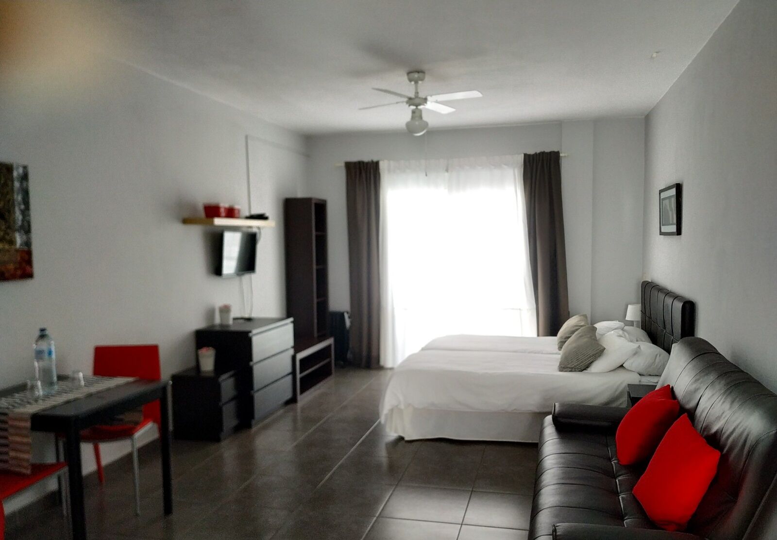 Una habitación de hotel con cama, escritorio, silla, televisión y ventilador de techo.