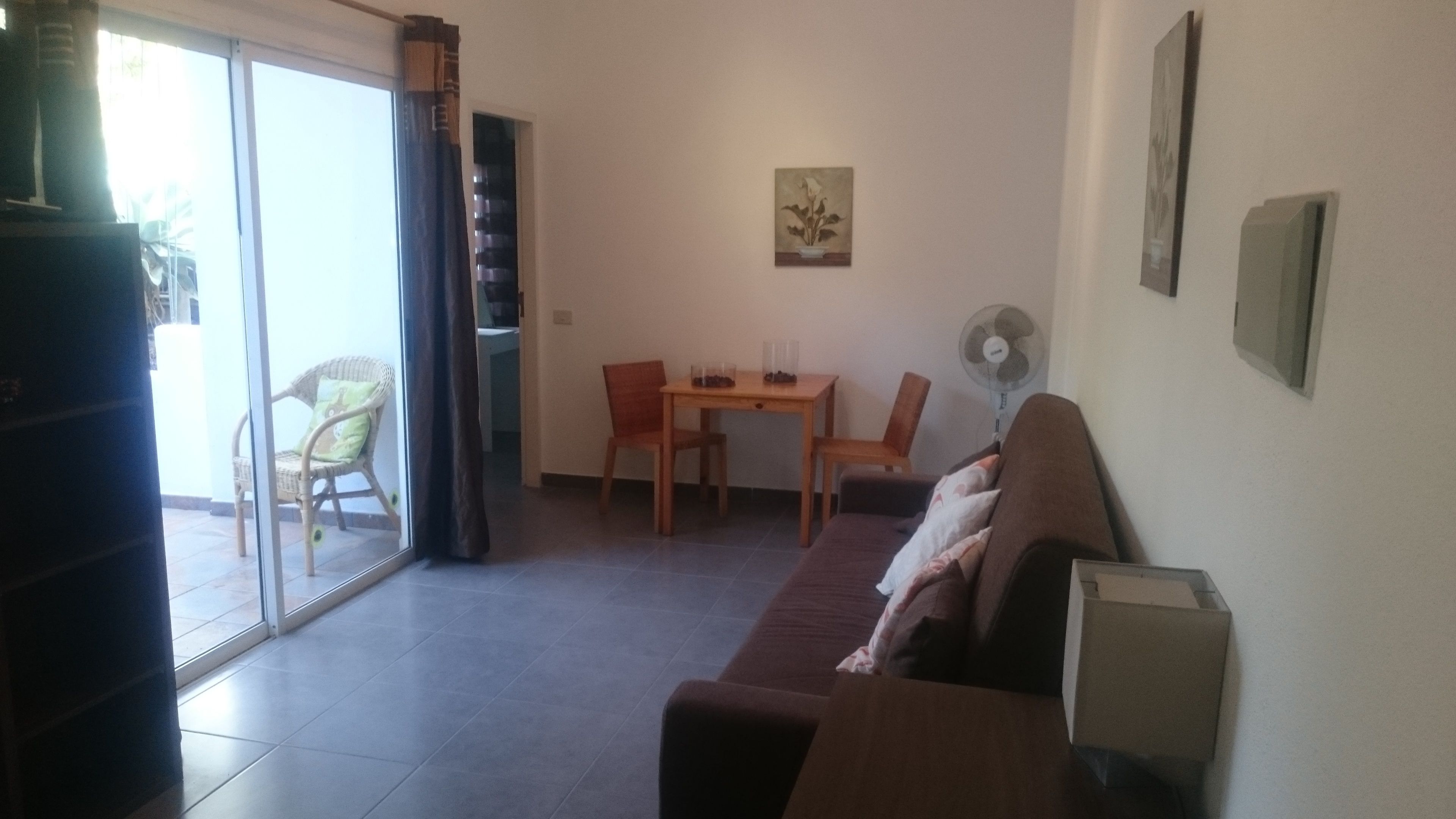 A living room with a sofa, a dining table with chairs, a fan, and a sliding glass door leading to an outdoor area.
