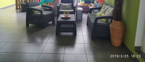Un patio interior amplio con mobiliario de mimbre, suelo de baldosas y valla de madera.