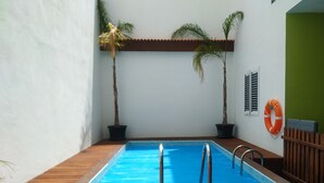 Una piscina interior con cubierta de madera, dos palmeras en macetas y un flotador en la pared.