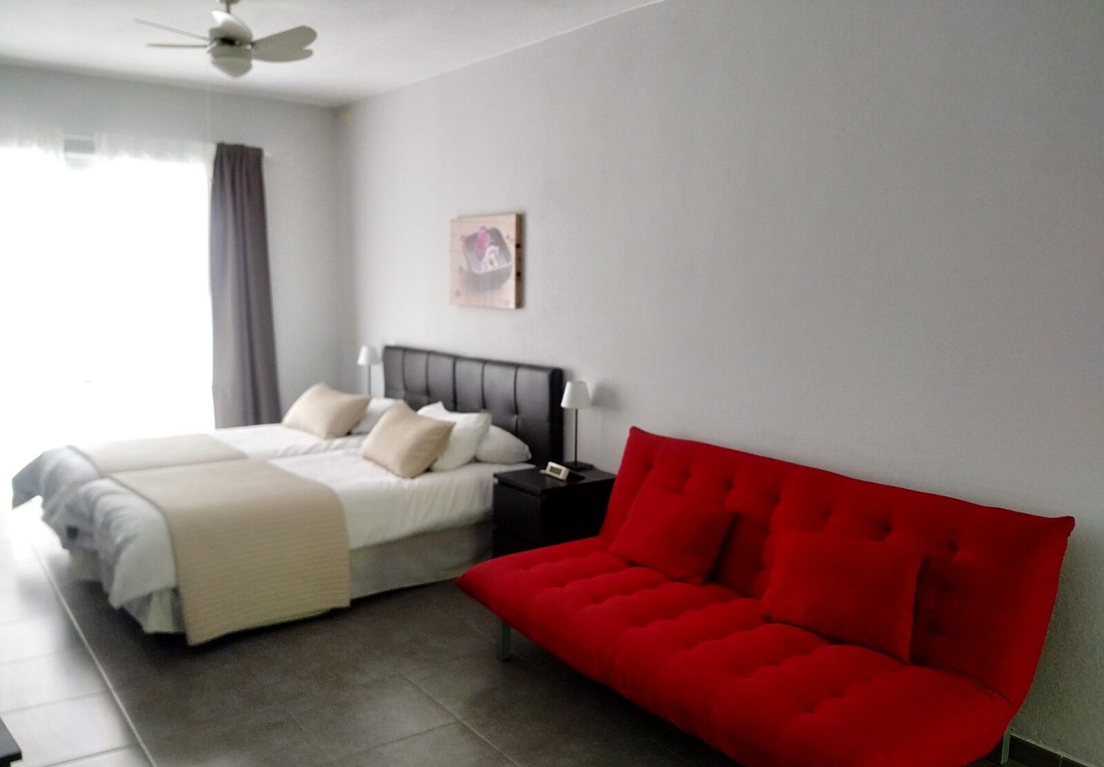 Ein Schlafzimmer mit einem Bett, einem roten Sofa, einem Nachttisch, einer Lampe und einem Deckenventilator.