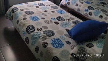 Una habitación pequeña y sencilla con dos camas, una ventana con cortinas y una mesita con una planta.