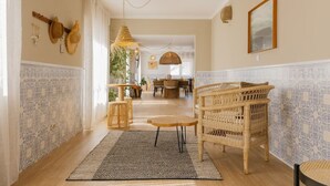 A spacious hallway with a rattan chair, a patterned rug, and a dining area in the background. - Camarao (Mafra)
