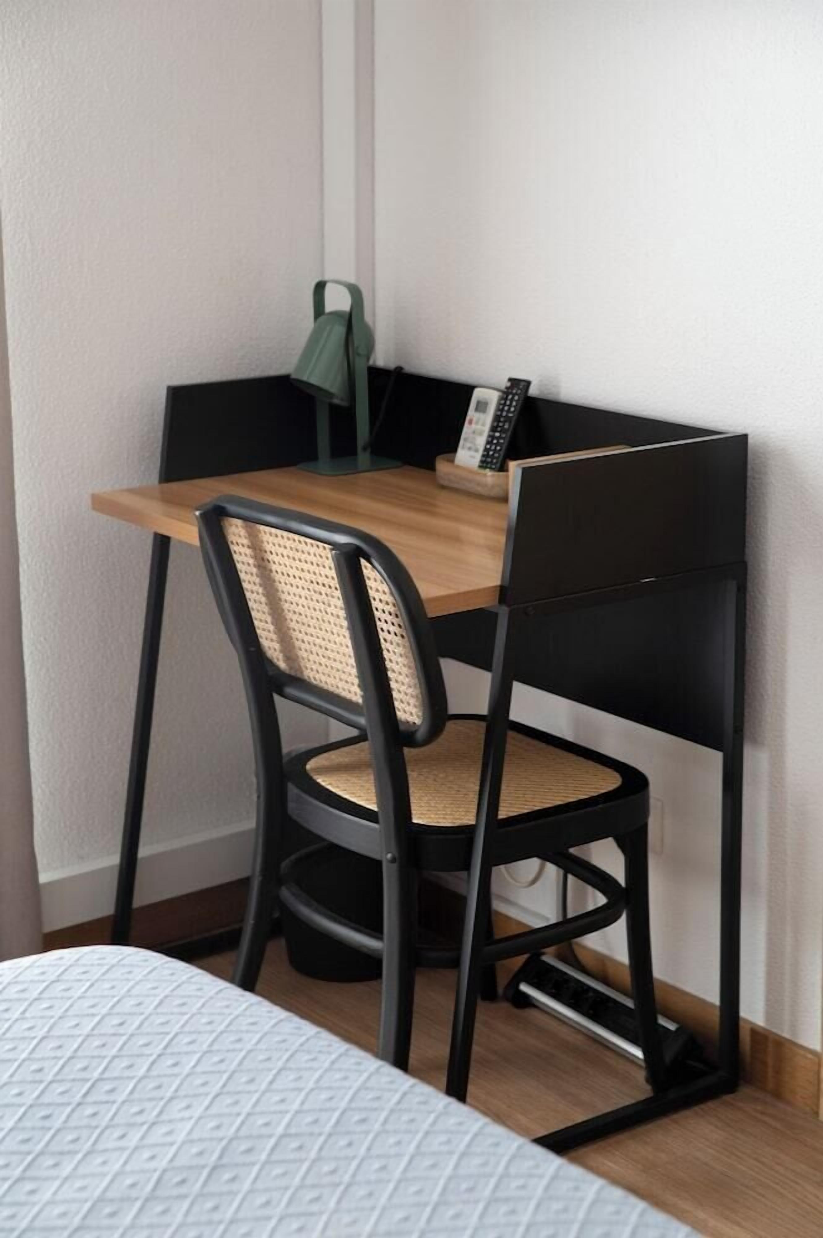 Een hoekbureau met een houten blad, twee zwarte stoelen met geweven zittingen, en een groene lamp.