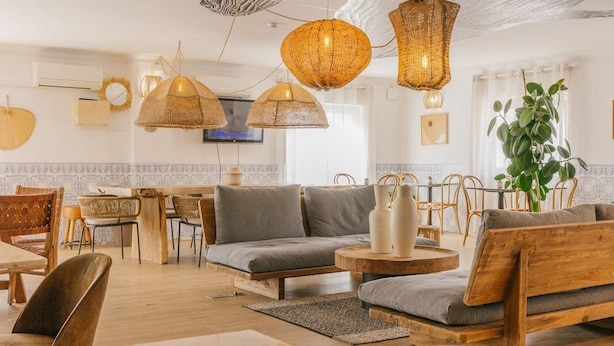 A cozy, well-lit dining area with wooden furniture, woven pendant lights, and a large plant. - Camarao (Mafra)