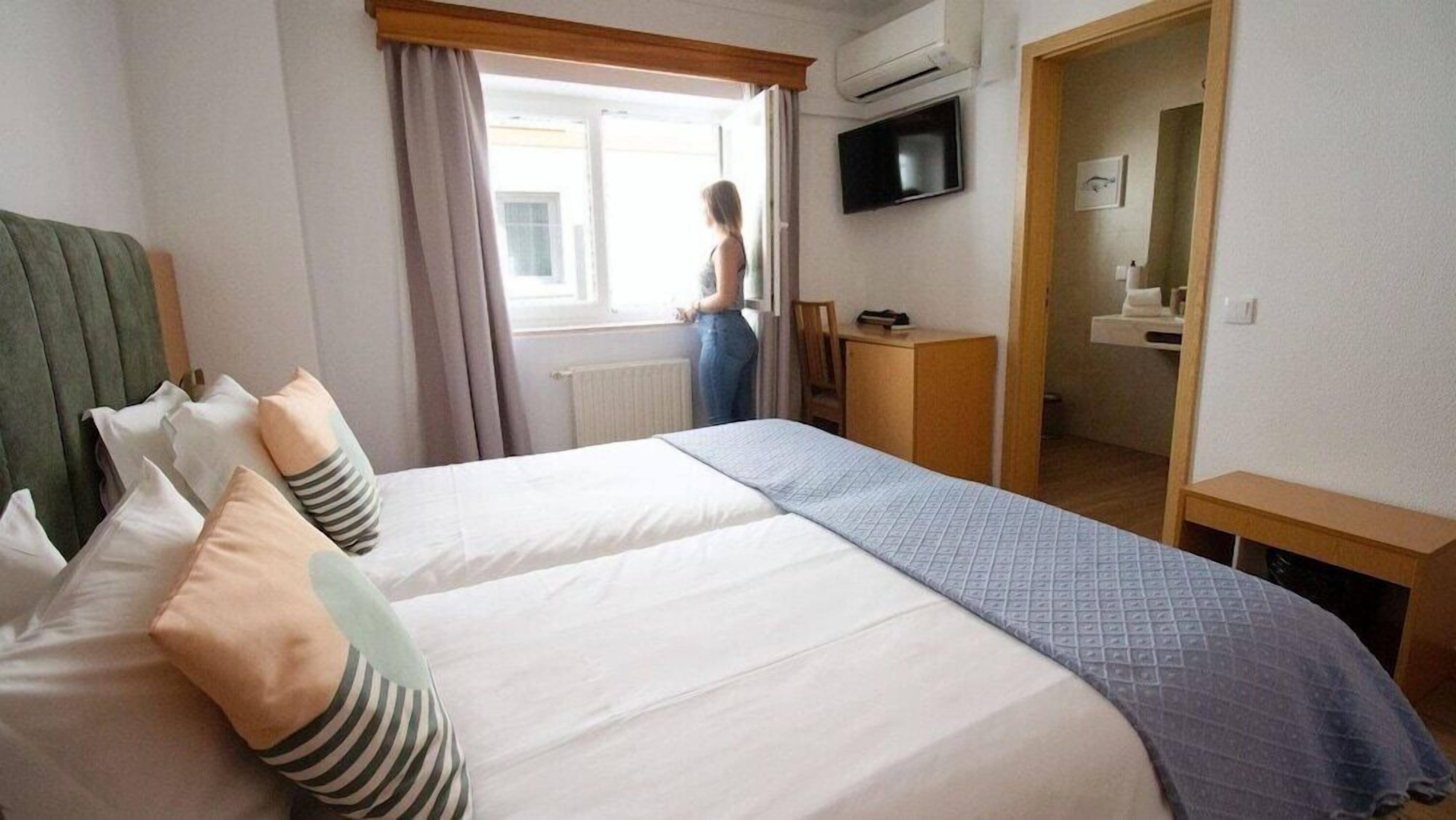 Habitación de hotel con dos camas, televisión, escritorio y baño visible a través de una puerta abierta.