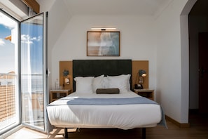 A modern hotel room with a large bed, a view through a glass door, a painting above the bed, and a nightstand with a lamp. - Camarao (Mafra)