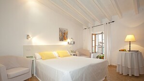 Hotelkamer met een groot bed, een nachtkastje, een stoel, een raam met gordijnen en een lamp op een bijzettafeltje.