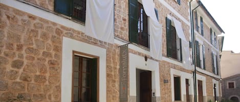 A stone building with multiple windows and doors, some with shutters. There are potted plants along the front.