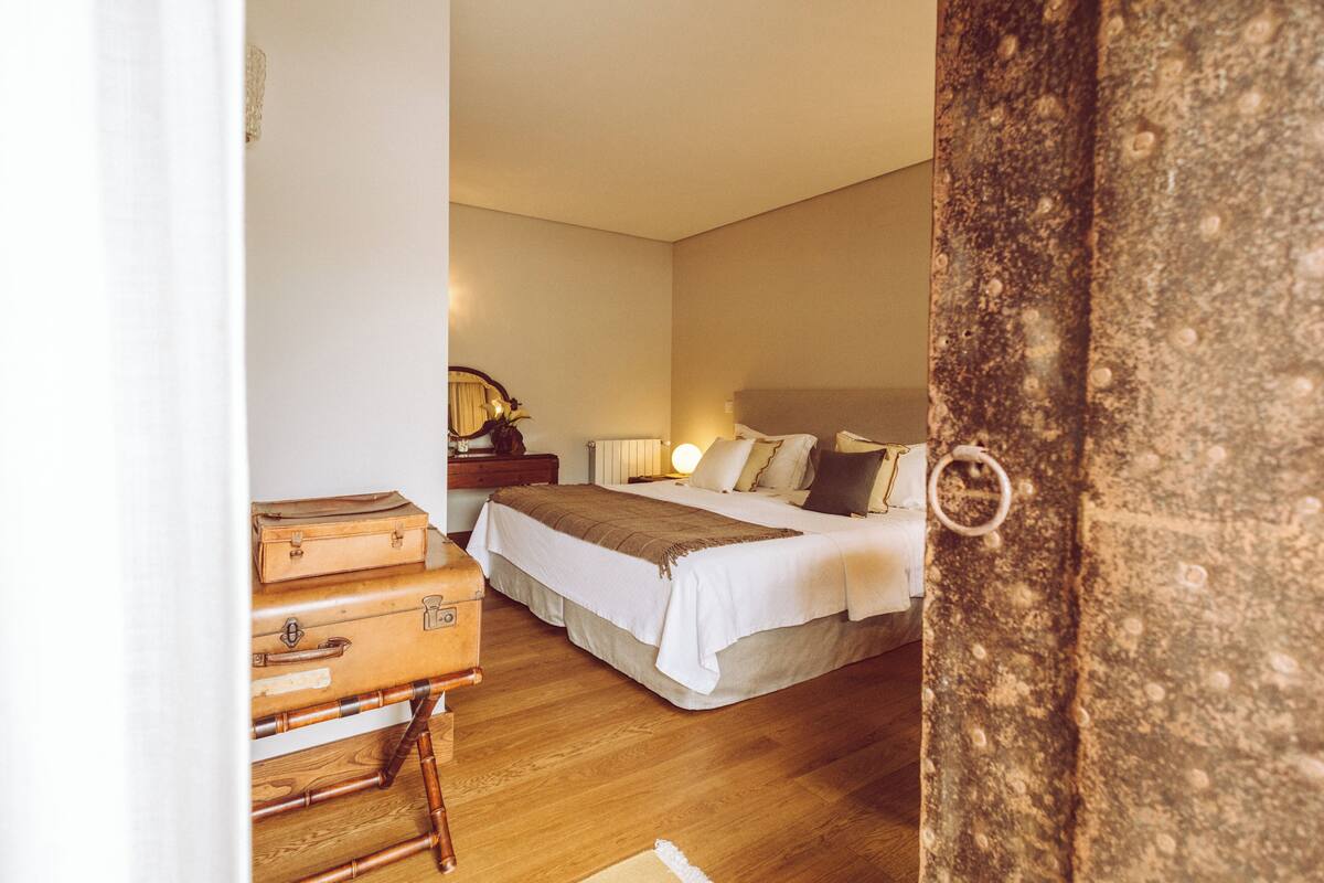 Une chambre d’hôtel avec un lit, une table de chevet, une lampe et une valise posée sur le sol.