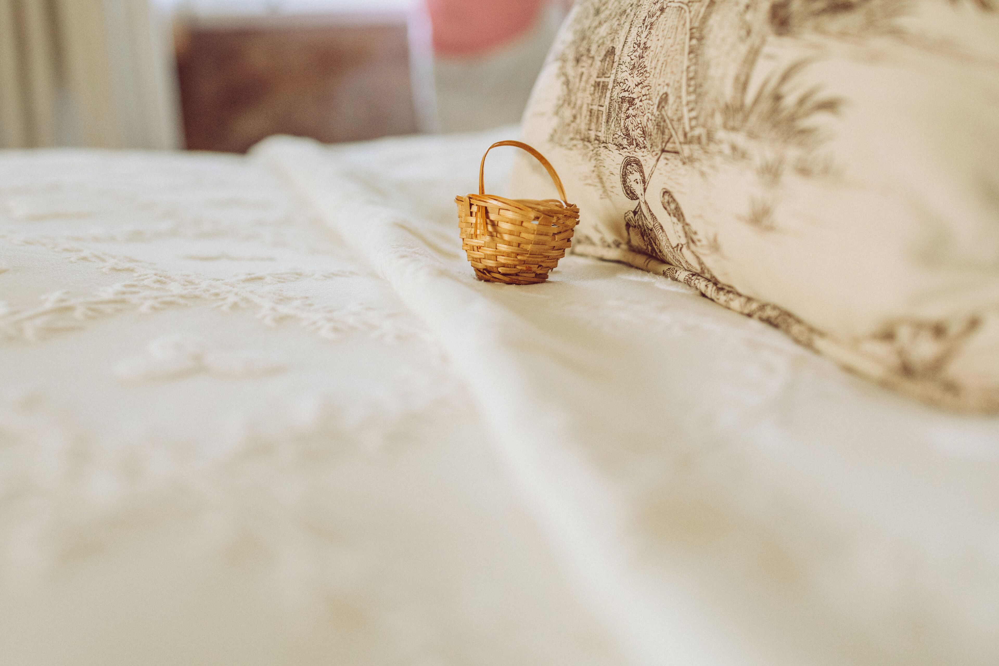 Una pequeña cesta tejida sobre una cama con un cojín estampado con motivos florales.