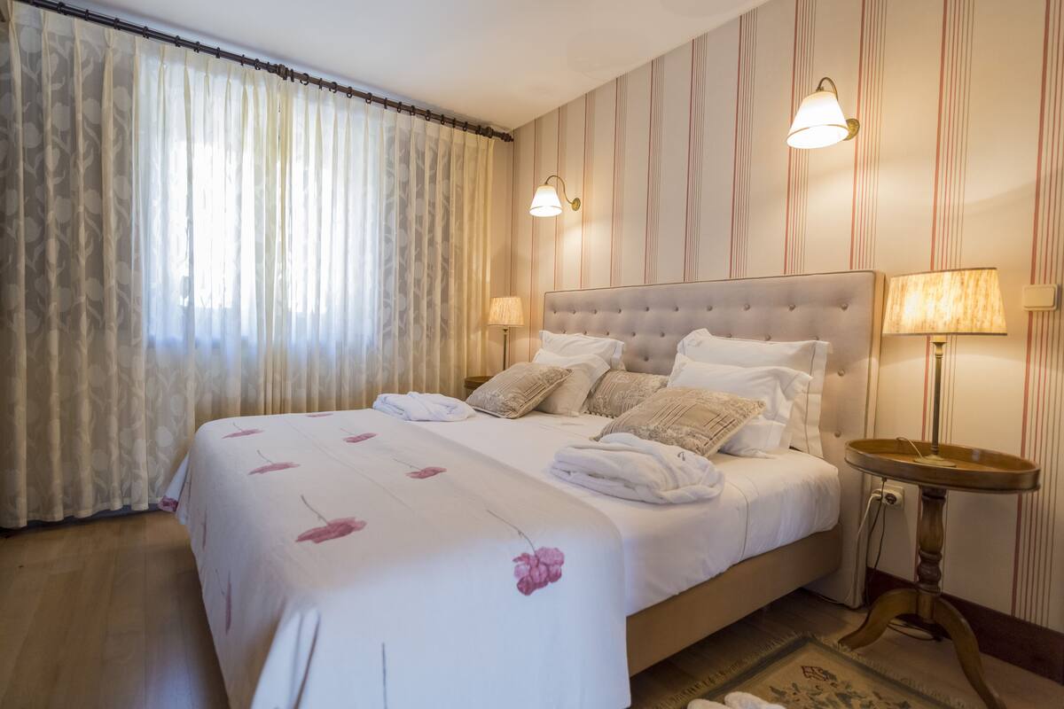 Un lit bien fait, recouvert d’une couvre-lit à motifs floraux, avec deux lampes de chevet et une table de nuit en bois.