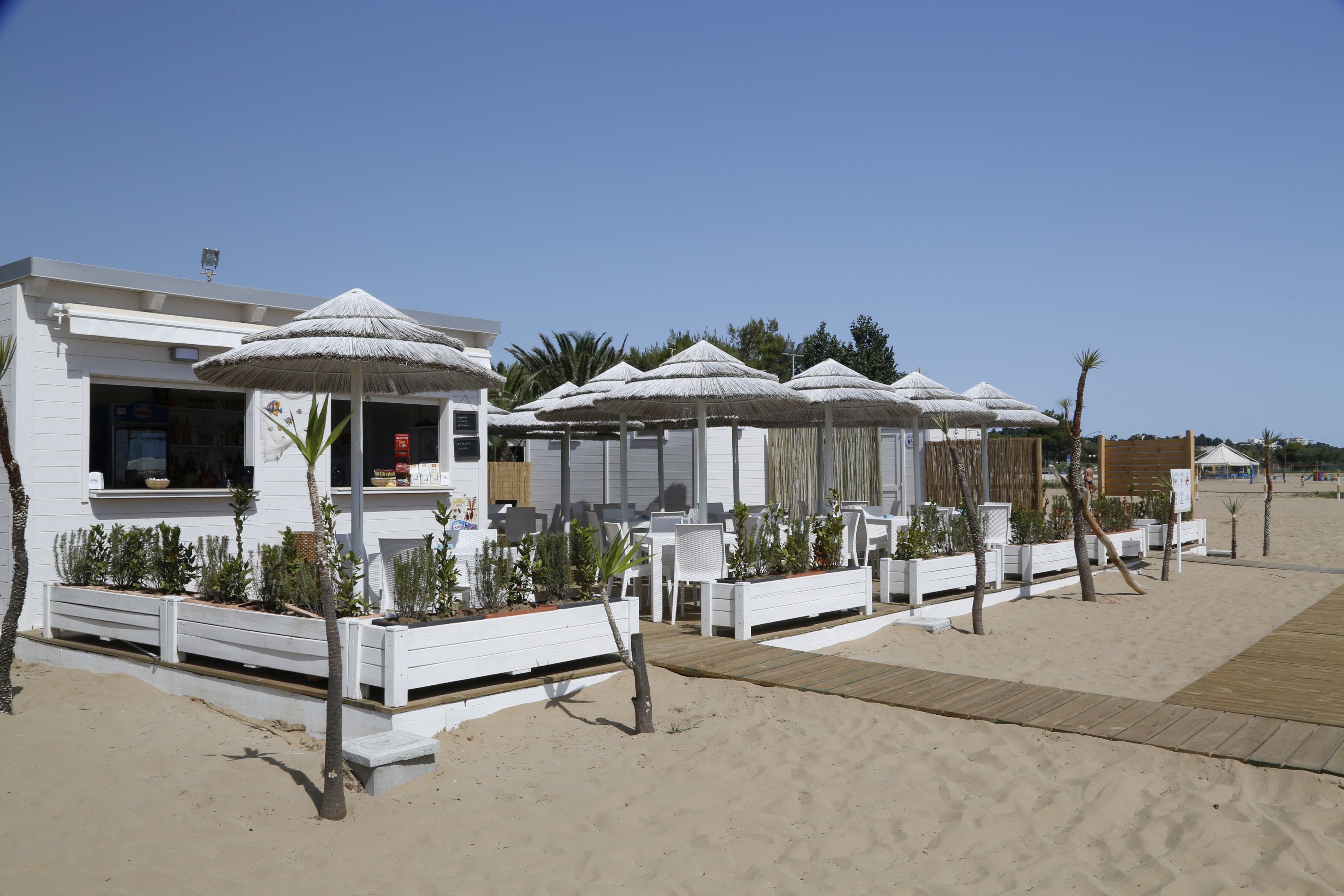 Un resort frente a la playa con áreas de estar al aire libre, edificios blancos y sombrillas de paja.
