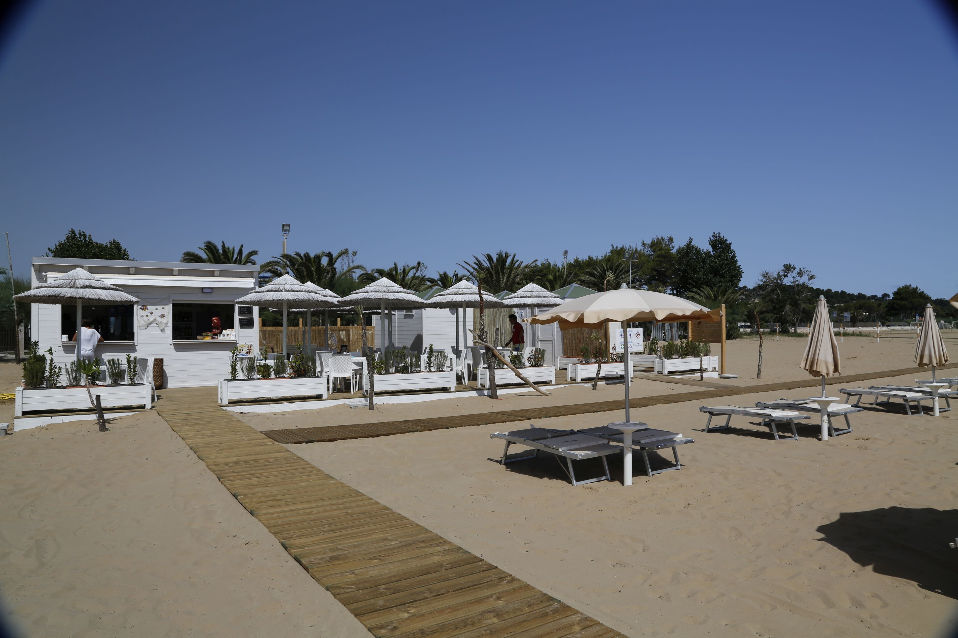 Un ristorante sulla spiaggia con posti a sedere all'aperto, un pontile in legno e ombrelloni.
