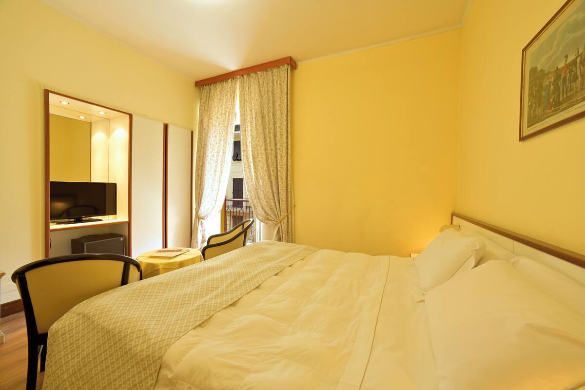 Een hotelkamer met een bed, bureau, stoel, klein tafeltje, spiegel en raam met gordijnen.