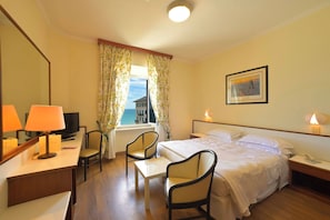 Habitación de hotel con una cama, dos sillas, un escritorio con lámpara, televisión y ventana con cortinas.