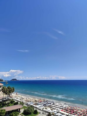 Un resort frente a la playa con vista al océano, un puerto deportivo y una hilera de sombrillas.