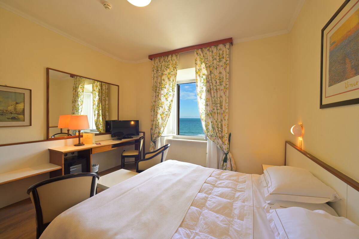 Een hotelkamer met een bed, bureau, stoel, televisie en uitzicht op zee.