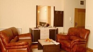A room with two leather sofas, a small table with a fruit bowl, a mirror, and a wooden door. - Premier Hotel (Skopje)