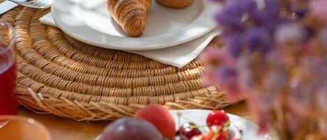 A breakfast setting with croissants on a plate, a bowl of fruit, and a glass of orange juice.