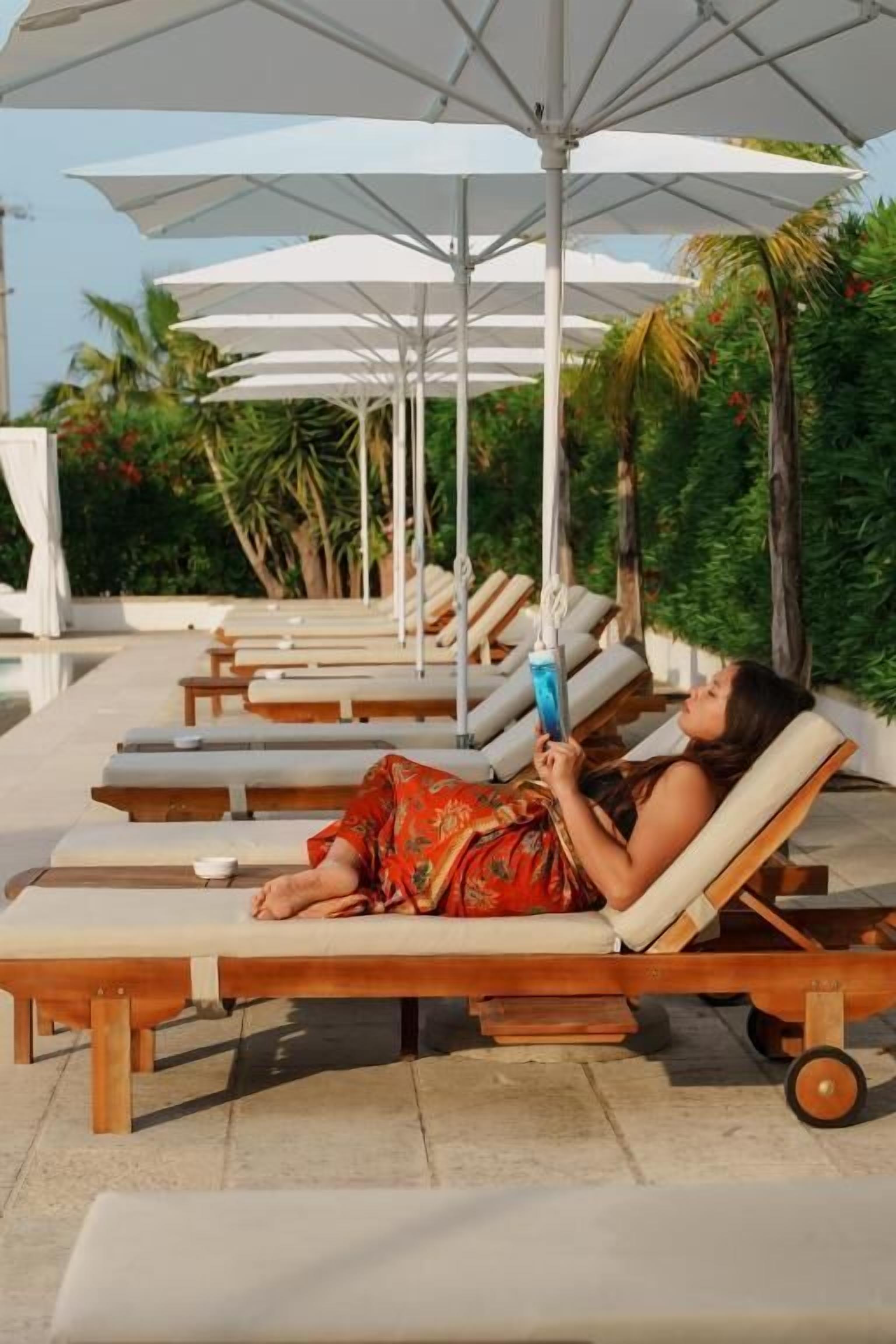 A poolside area with lounge chairs and umbrellas, surrounded by greenery.