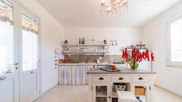 A kitchen with white cabinetry, a chandelier, and a window with curtains.