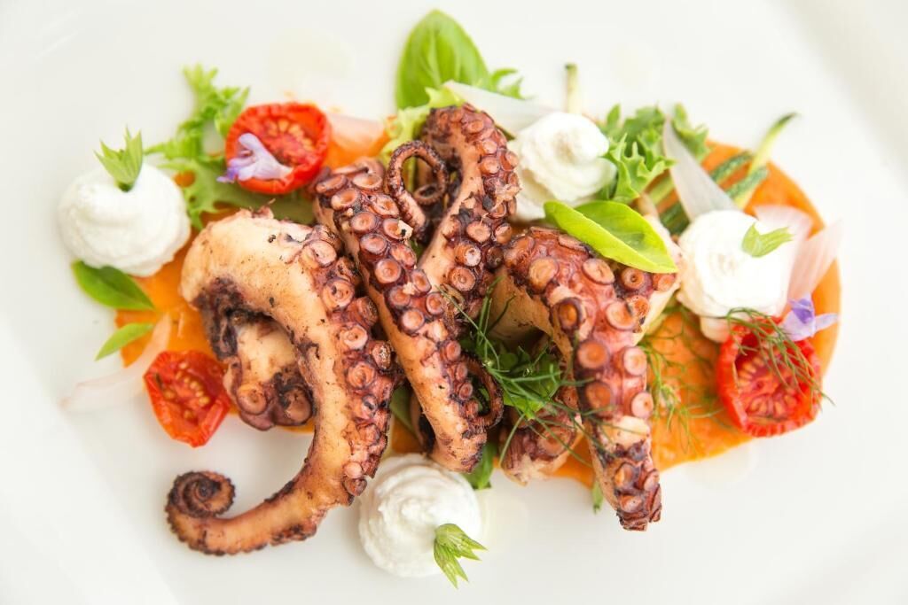 A dish of grilled octopus with vegetables and a creamy sauce.