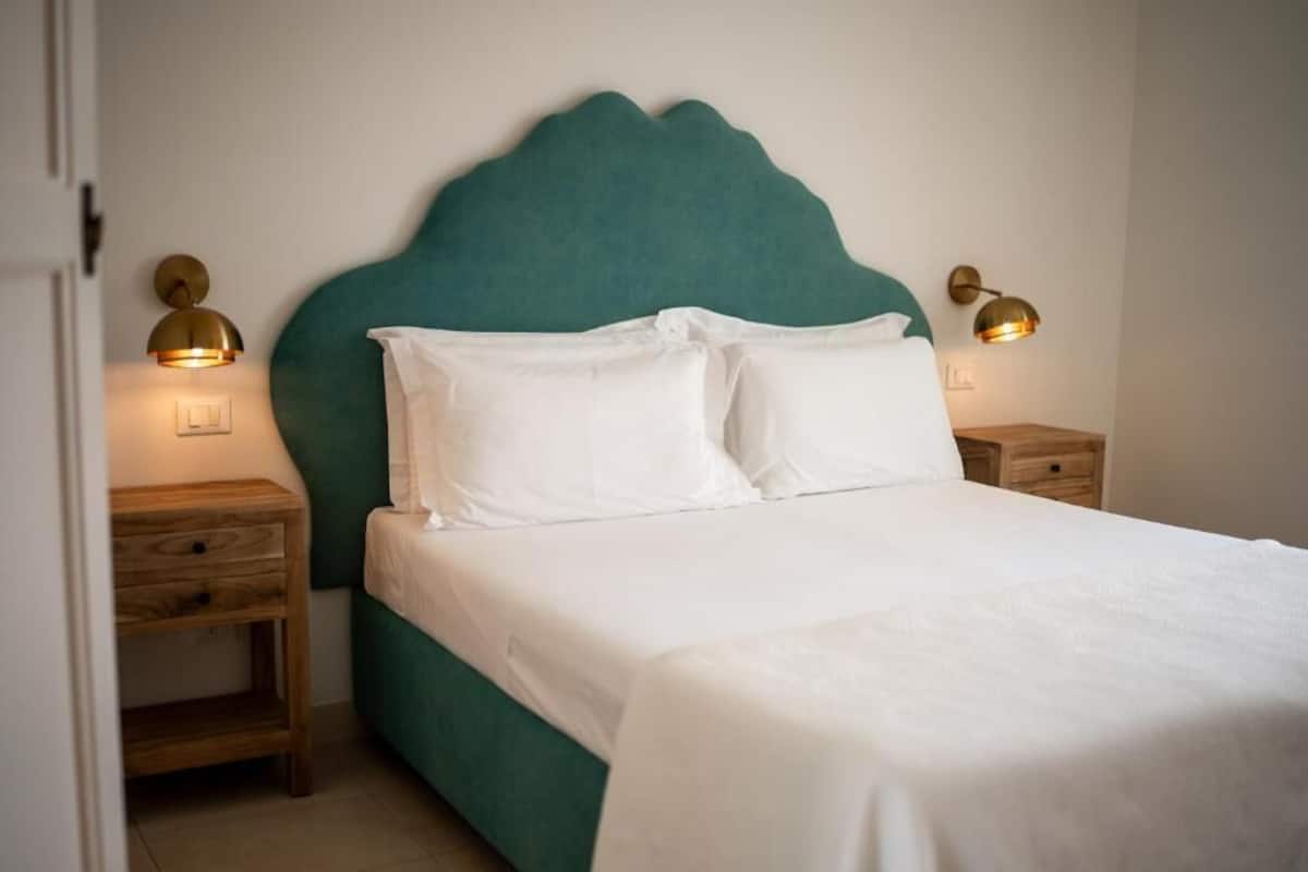A neatly made bed with white linens and a teal headboard, flanked by two bedside tables with lamps.