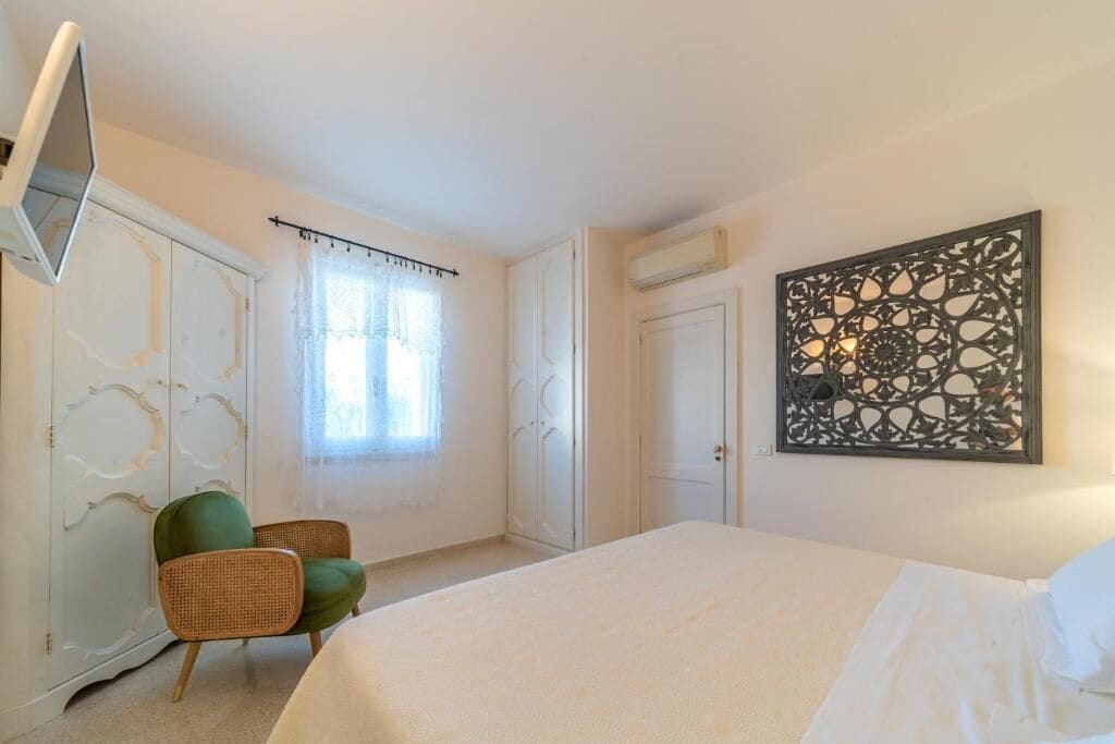 A bedroom with a bed, a green chair, a decorative wall piece, and a partially open wardrobe.