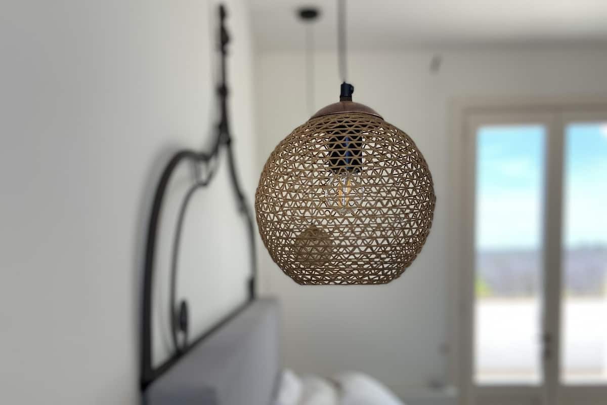 A bedroom with a bed, a hanging light fixture, and a window with a view.