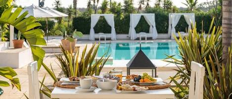 A dining table with breakfast items and a view of a swimming pool.