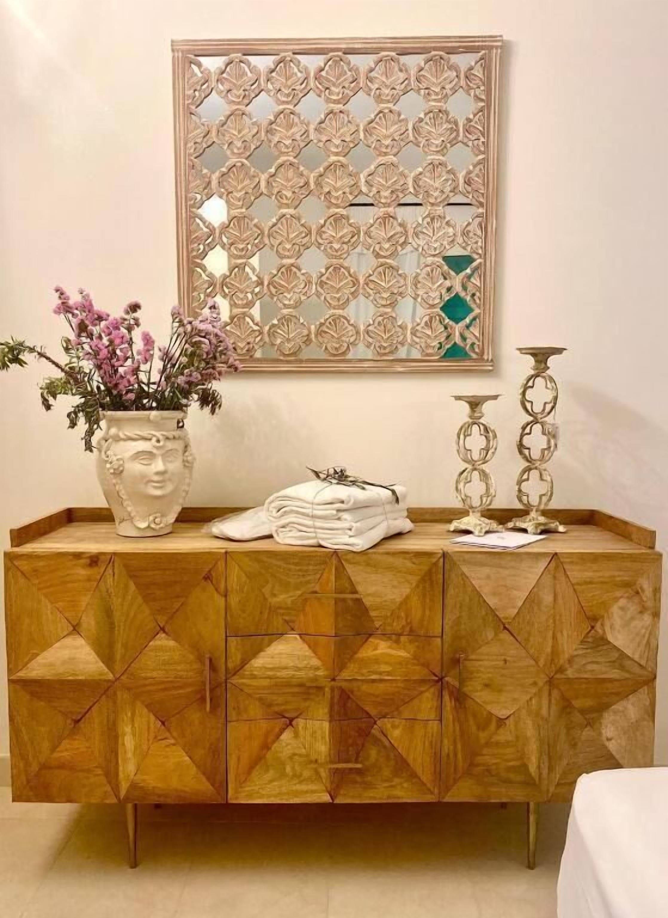 A wooden cabinet with geometric patterns, a vase with flowers, and a decorative mirror above it.