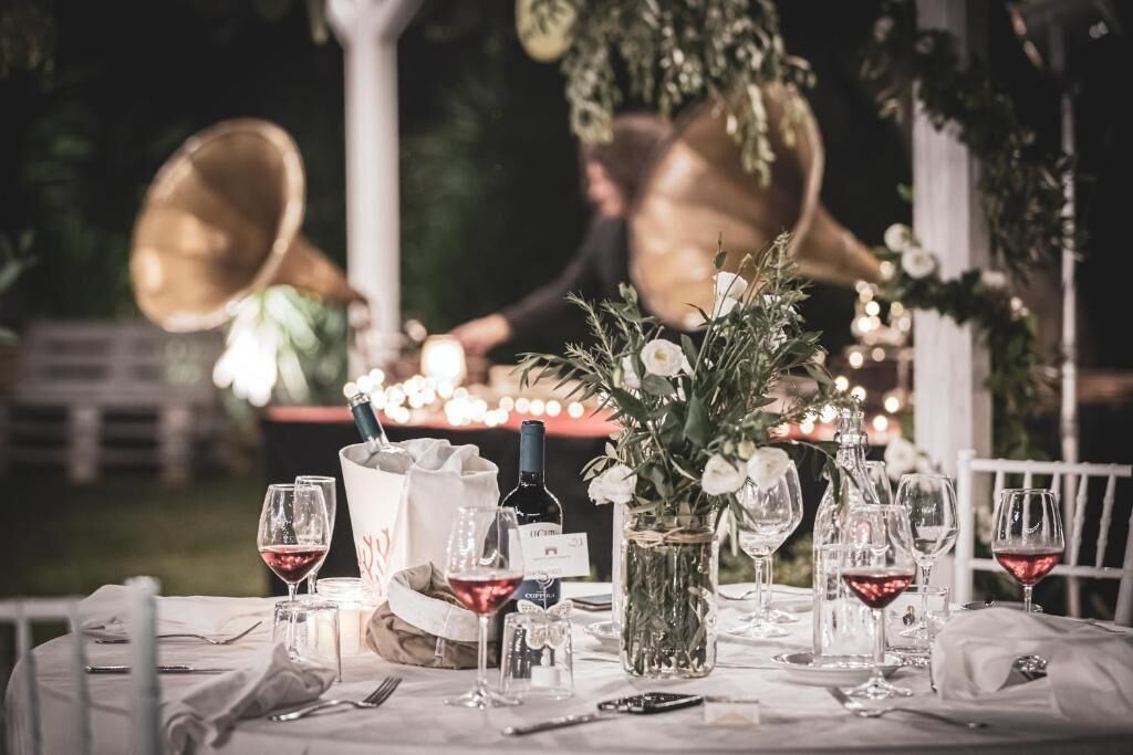 A table set for a formal outdoor event with a bottle of wine, glasses, and a vase of flowers.