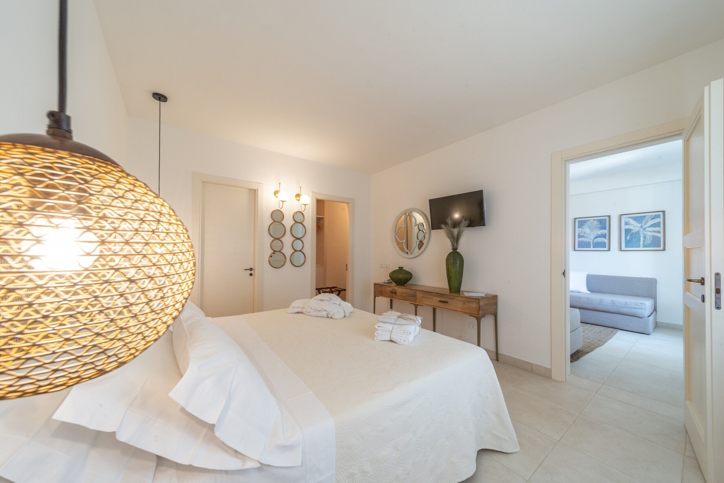 A hotel room with a large bed, a bedside table with a vase, a wall-mounted TV, and a door leading to a balcony.