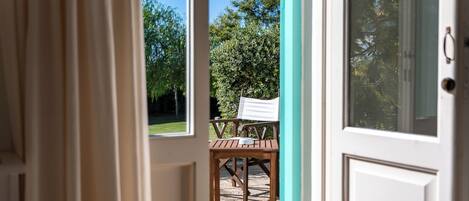 An open door leading to a patio with a wooden table and chairs, a view of greenery, and a white door with a glass panel.