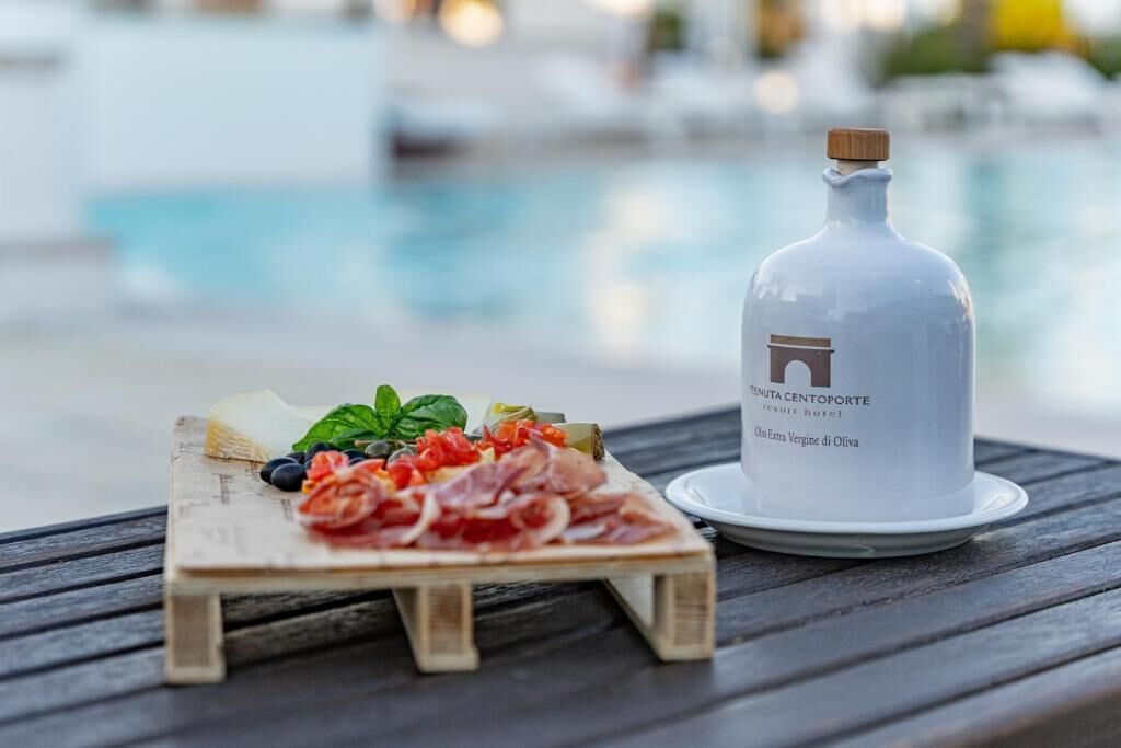 A wooden serving board with a variety of cured meats, cheeses, and vegetables, accompanied by a bottle of olive oil.
