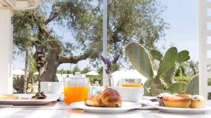 A breakfast table with croissants, muffins, and orange juice, set outdoors with cacti and trees in the background. - Tenuta Centoporte (Giurdignano)