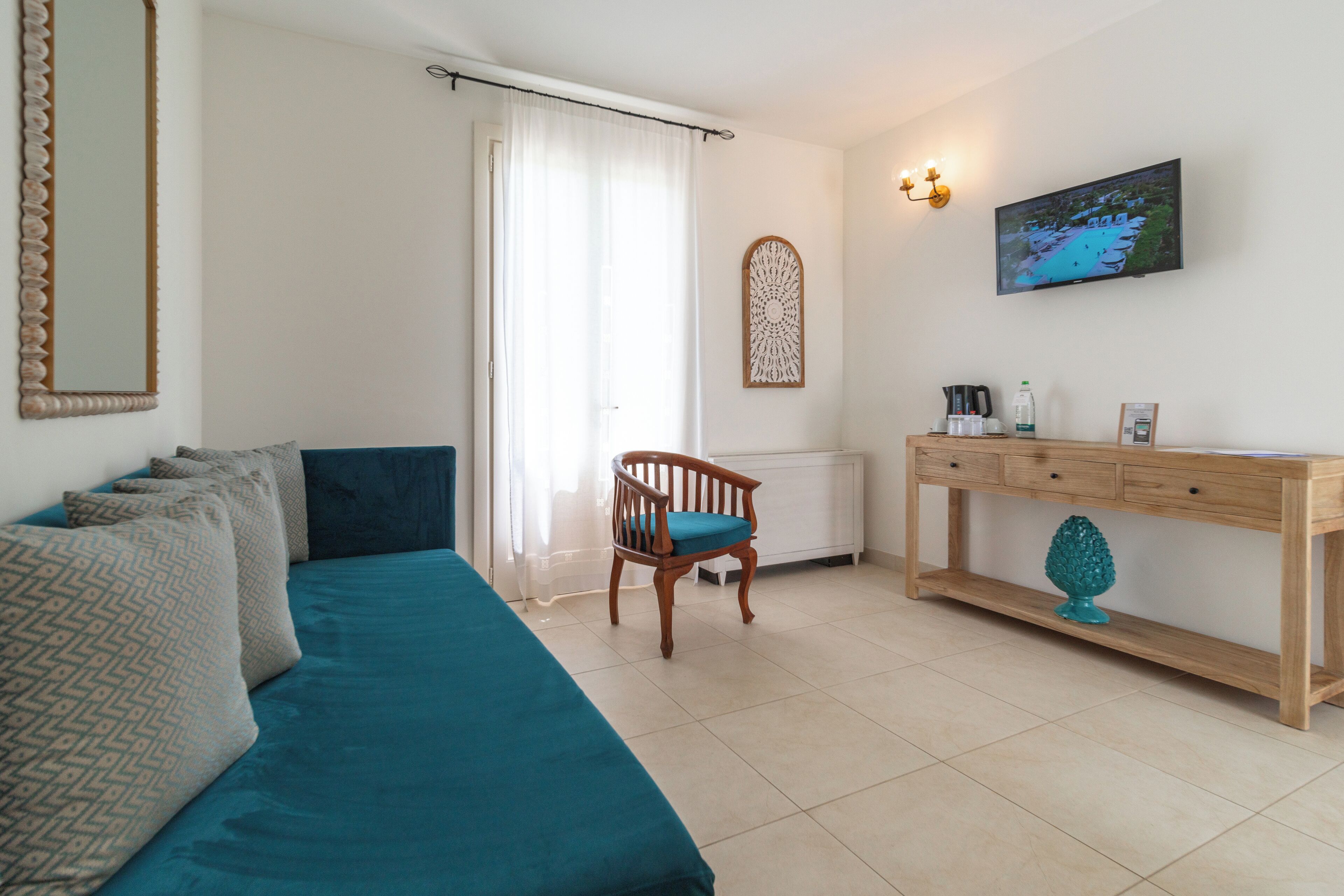 Une pièce comprenant un lit, une chaise, une console en bois, un téléviseur et un élément décoratif mural.