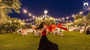 A woman in a black dress dancing outdoors at night with string lights and trees in the background. - Tenuta Centoporte (Giurdignano)