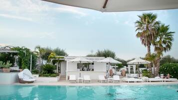 Ein Poolbereich mit Liegestühlen, Sonnenschirmen und einer Bar.