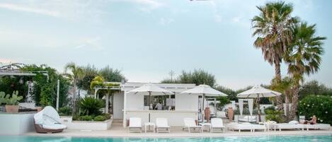 A pool area with lounge chairs, umbrellas, and a bar.