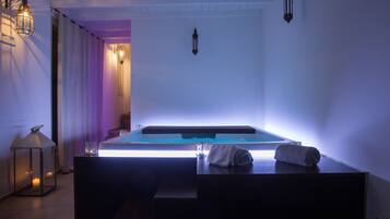 Ein Wellnessraum mit Whirlpool, einem Glastisch mit Handtüchern und Wandleuchtern.