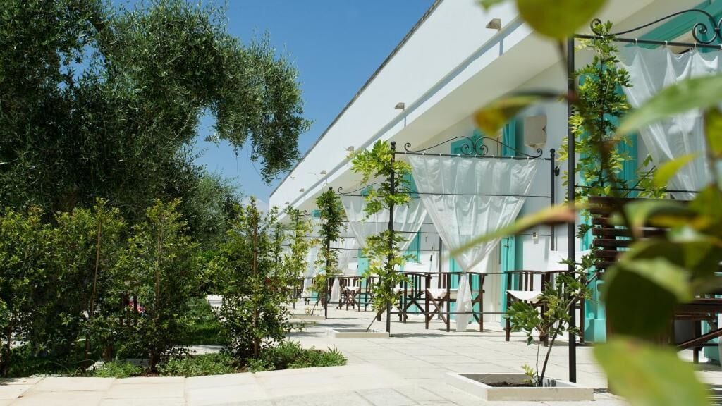A courtyard with outdoor seating, trees, and a building with a white facade and teal accents.