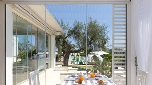 A dining area with a table set for breakfast, overlooking a pool and garden. - Tenuta Centoporte (Giurdignano)